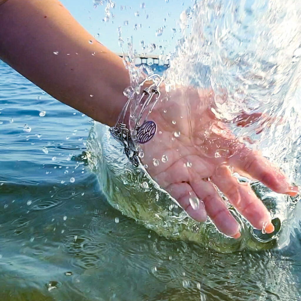 Photo of hand splashing in water with stainless steel water themed bracelets on wrist