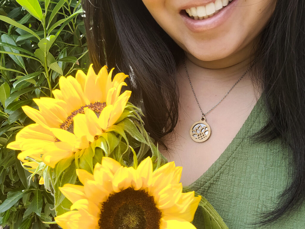 Artist wearing handmade bamboo and stainless steel sunflower necklace and holding sunflowers